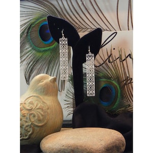 May include: A pair of silver dangle earrings with a delicate, intricate design. The earrings are long and rectangular in shape, with a filigree pattern.