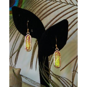 May include: A pair of gold dangle earrings with iridescent oval-shaped glass stones. The stones have a yellow, green, and pink color.