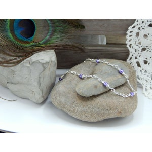 May include: A silver chain necklace with purple beads. The necklace is displayed on a gray rock.