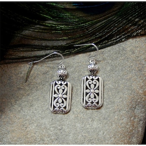 May include: Silver dangle earrings with a rectangular design featuring a cutout floral pattern.