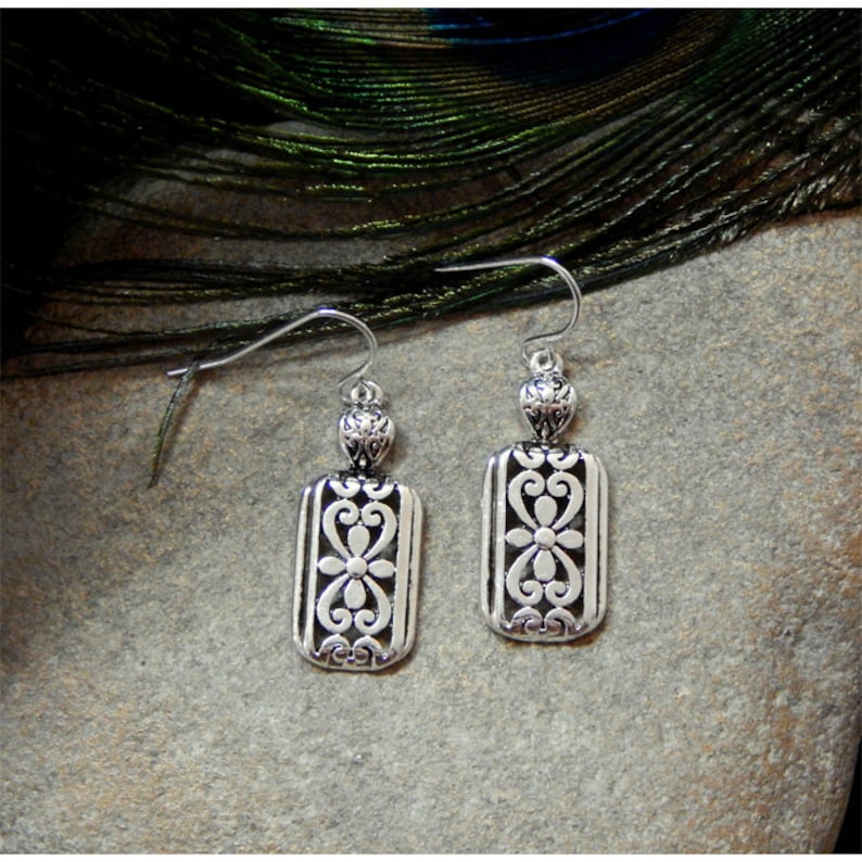 May include: Silver dangle earrings with a rectangular design featuring a cutout floral pattern.