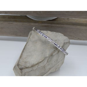 May include: A silver bangle bracelet with an intricate design of swirls and an infinity symbol.