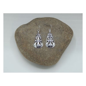 May include: A pair of silver dangle earrings with a delicate floral design. The earrings are hanging from a rock.