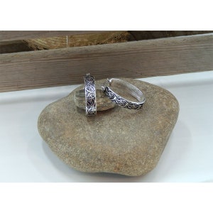 Puede incluir: Un par de pendientes de aro de plata con un intrincado dise&ntilde;o floral. Los pendientes son de forma ovalada y tienen un acabado de esmalte negro.