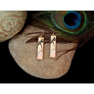 May include: A pair of dangle earrings with a dragonfly design. The earrings are made of metal and have a copper and white finish.