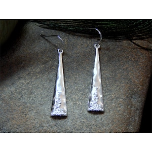 May include: A pair of silver dangle earrings with a teardrop shape and a decorative design at the bottom. The earrings have a shiny finish.