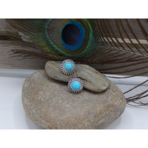 May include: A pair of silver earrings with turquoise stones set in a circular design.