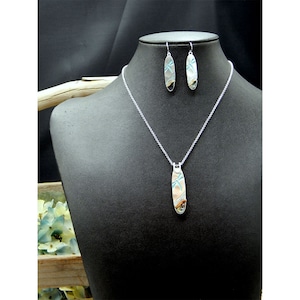 May include: A silver necklace and earrings set with a dragonfly pendant and matching earrings. The dragonfly design is embossed and features blue accents.