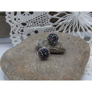 May include: A pair of silver stud earrings with round, iridescent agate stones. The stones have a dark purple, green, and gold color.