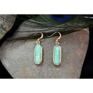 May include: A pair of gold dangle earrings with oval-shaped turquoise blue stones. The stones have a shimmery, iridescent finish.