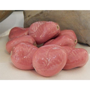 May include: A group of pink ceramic beads with a smooth, glossy finish. The beads are shaped like leaves and have a slightly irregular shape.