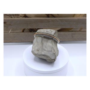 May include: A hinged cuff bracelet featuring a central twisted rose gold-tone band flanked by two silver-tone beaded bands. The bracelet has a textured finish and a metallic construction, displaying a combination of silver and rose gold colors.