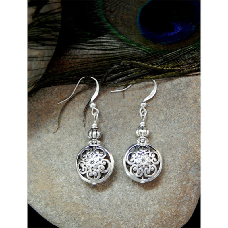 May include: Silver dangle earrings with a round, filigree design and a small bead at the top of the drop.