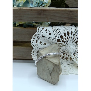 Puede incluir: Un brazalete de plata con un intrincado dise&ntilde;o floral. El brazalete se muestra sobre una peque&ntilde;a roca gris.