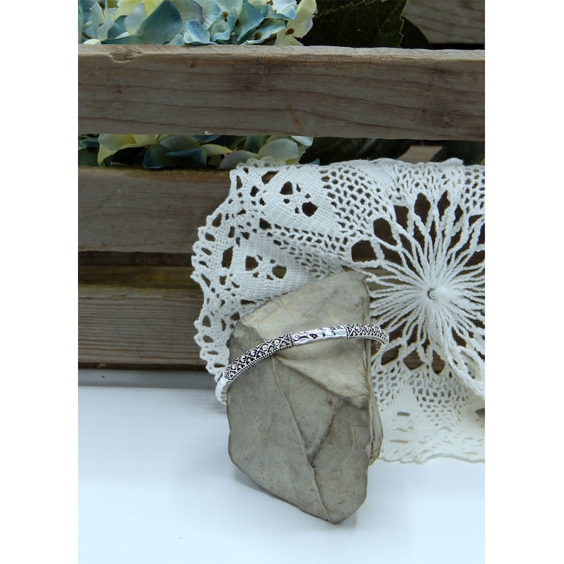 Puede incluir: Un brazalete de plata con un intrincado dise&ntilde;o floral. El brazalete se muestra sobre una peque&ntilde;a roca gris.