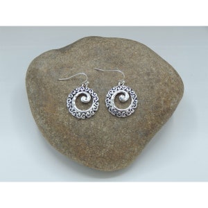 K&ouml;nnte beinhalten: Ein Paar silberfarbene Ohrringe mit einem Spiraldesign. Jeder Ohrring hat einen kreisf&ouml;rmigen Rahmen mit einem Wirbelmuster um eine zentrale Spirale. Die Ohrringe haben einen Hakenverschluss.