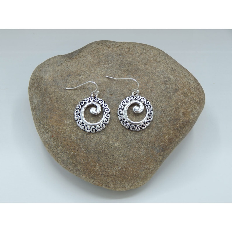 K&ouml;nnte beinhalten: Ein Paar silberfarbene Ohrringe mit einem Spiraldesign. Jeder Ohrring hat einen kreisf&ouml;rmigen Rahmen mit einem Wirbelmuster um eine zentrale Spirale. Die Ohrringe haben einen Hakenverschluss.