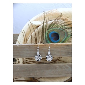 May include: A pair of silver-toned dangle earrings featuring circular charms with intricate openwork scroll patterns. Each earring is suspended from a simple hook wire and includes a small, textured silver bead accent above the circular charm.