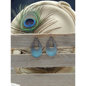 Puede incluir: Un par de pendientes colgantes de color azul turquesa con un acabado texturizado martillado. Los pendientes tienen forma de l&aacute;grima con un corte en el centro.