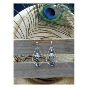 May include: A pair of silver dangle earrings with a teardrop shape. The earrings feature a black bead with a silver floral design and smaller black beads.