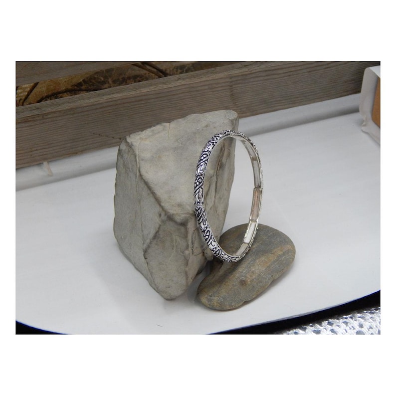 May include: Silver bangle bracelet with an intricate, detailed design. The bracelet is open and has a hinged closure.