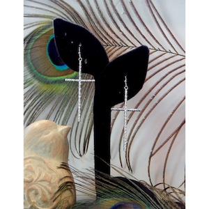 May include: Silver cross dangle earrings with a textured finish. The earrings are displayed on a black velvet stand.