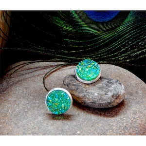 May include: A pair of silver earrings with green glitter embedded in the center of each earring.
