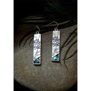 May include: Silver dangle earrings with a rectangular design featuring a black tree silhouette and a blue and green abalone shell inlay.