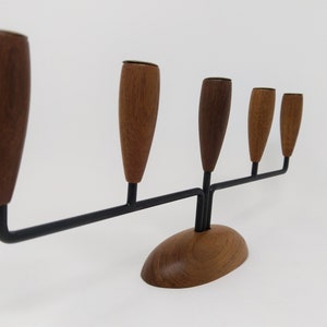 May include: A five-arm wooden and metal candle holder with a brown wooden base and arms. The candle holders are made of wood and have a brown finish.