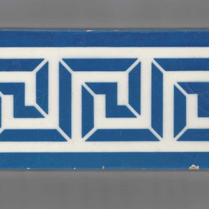 May include: A blue and white ceramic tile with a repeating geometric pattern. The pattern is a series of interlocking squares and rectangles, creating a Greek key design.