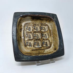 Peut inclure: Un plat carré en céramique avec un glaçage bleu et un intérieur blanc. L'intérieur présente un motif en relief de neuf carrés avec un chiffre "4" dans chaque carré.