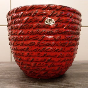 May include: Red ceramic planter with a woven pattern and a label that says "U Keramik".