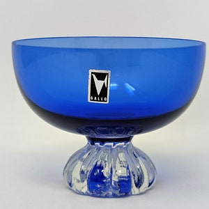 May include: A cobalt blue glass bowl with a clear glass pedestal base. The bowl has a label that reads "Gallo".