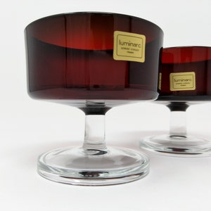 Può includere: Due coppe da dessert in vetro trasparente con una ciotola rosso scuro e un gambo e una base trasparenti. Le coppe hanno un'etichetta dorata con la scritta "luminarc".