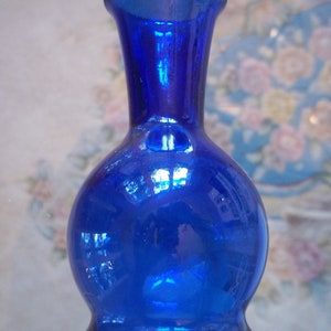May include: A small, cobalt blue glass vase with a round body and a narrow neck. The vase has a shiny, reflective surface.