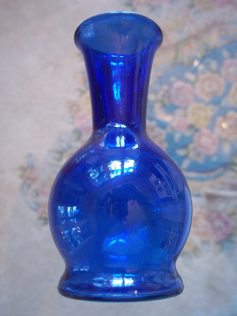 May include: A small, cobalt blue glass vase with a round body and a narrow neck. The vase has a shiny, reflective surface.