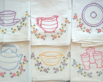 May include: Six white tea towels with embroidered floral designs. Each towel features a different design, including a teacup, pitcher, bowl, and a set of three mugs.