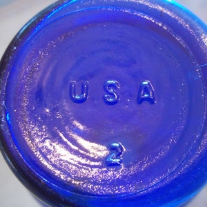 May include: A close-up of a cobalt blue glass bottle with the word "USA" and the number "2" embossed on the bottom.