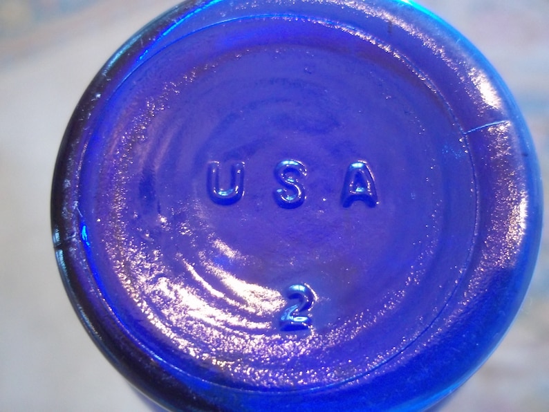May include: A close-up of a cobalt blue glass bottle with the word "USA" and the number "2" embossed on the bottom.