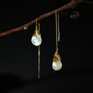 May include: A pair of gold chain earrings with white pearl-like drops. The pearls are wrapped in gold wire.