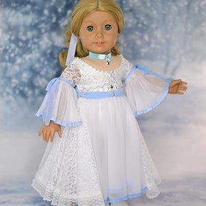 May include: A doll wearing a white lace dress with a light blue sash and matching collar. The doll has blonde hair and blue eyes. The background is a light blue with a snowy effect.