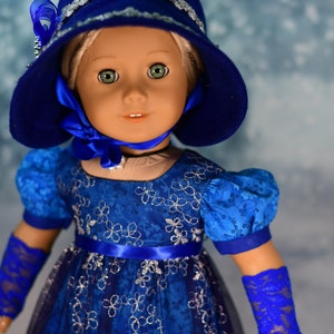 May include: A doll wearing a blue dress with silver floral embroidery, a blue hat with silver trim, and blue lace gloves.