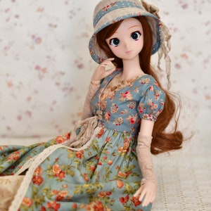 May include: A doll wearing a blue floral dress and matching hat. The dress features a pattern of red and orange flowers. The doll has long brown hair and is wearing lace gloves. The hat has a blue band with floral accents.