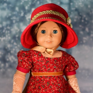 May include: A red doll wearing a red hat with gold trim and a red and green floral dress. The doll has blue eyes and brown hair.