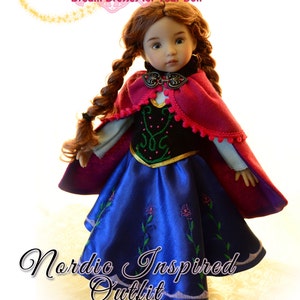 May include: A sewing pattern for a 13 inch doll outfit inspired by a Nordic design. The doll is wearing a blue dress with embroidered flowers, a black bodice, and a red cape with a gold trim. The pattern is titled "Nordic Inspired Outfit" and is for Dianna Effner's Little Darling dolls.
