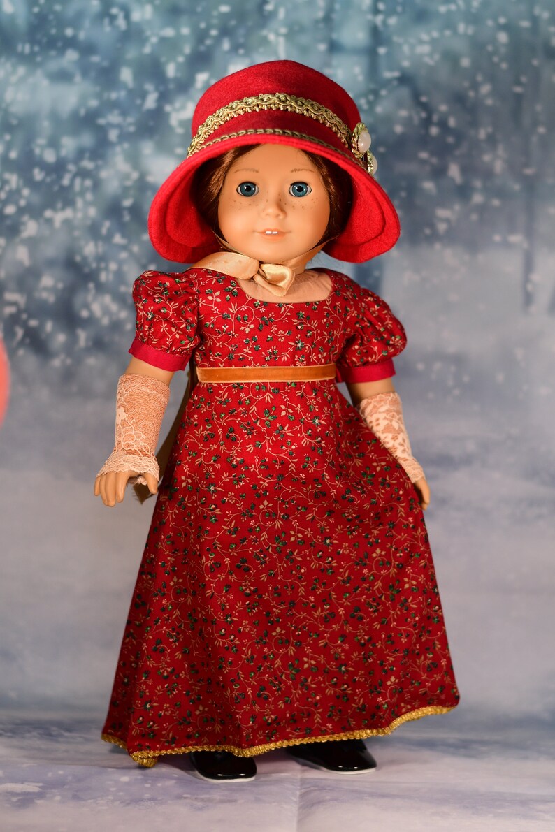 May include: A red dress with a floral pattern and gold trim. The dress is worn by a doll with a red hat and gold trim. The doll has blue eyes and a fair complexion.