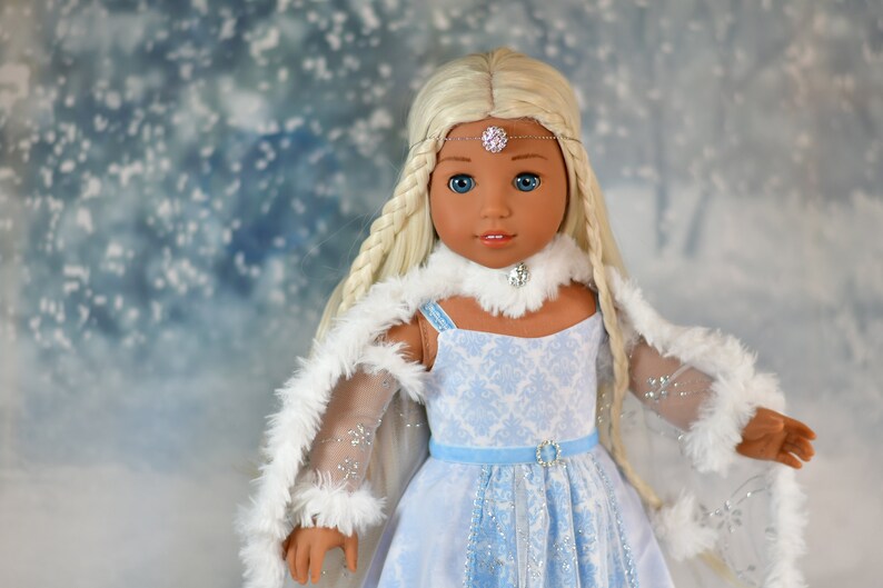 May include: A doll with long blonde braids wearing a blue and white dress with a white fur trim. She is wearing a silver tiara and a white fur collar.