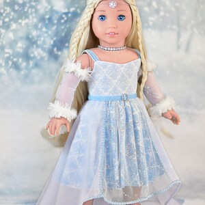May include: A doll wearing a light blue and white dress with a white fur trim on the sleeves. The doll has long blonde hair and blue eyes. The doll is wearing a silver tiara and a silver necklace. The doll is standing on a white background with a blue and white snowflake pattern.