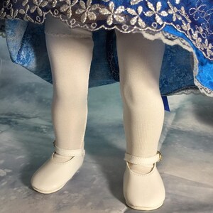 May include: White tights and white shoes with a buckle on a doll wearing a blue and silver dress.