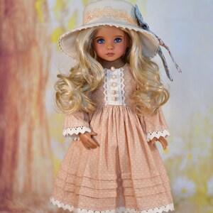 May include: A doll in a peach dress with white polka dots and lace detailing. The doll has long, wavy blonde hair, blue eyes, and a matching hat with a floral bow. The doll is wearing white shoes.